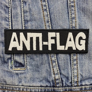 May include: Black and white embroidered patch with the text "ANTI-FLAG" on a denim jacket.