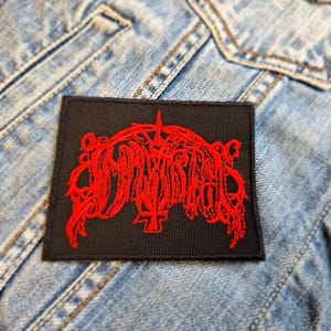 Könnte beinhalten: Schwarzer gestickter Patch mit einem roten Logo der Band Mayhem. Das Logo ist eine stilisierte Schriftart mit einem Schwert und einem Kreuz.