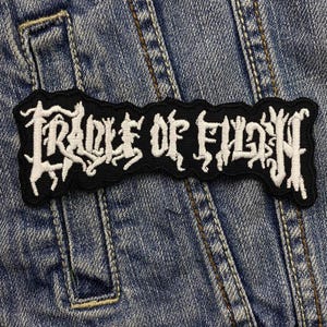 Op de afbeelding: Een geborduurde zwarte en witte patch met de tekst "Cradle of Filth" in een gotisch lettertype.