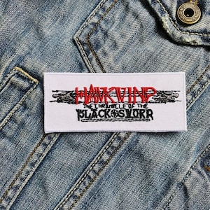 May include: A rectangular white patch with the text "HAWKWIND" in red, stylized lettering above "THE CHRONICLE OF THE BLACK SWORD" in black. The patch is set against a denim jacket.