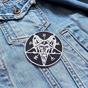 Peut inclure: Un écusson brodé noir et blanc d'un pentagramme avec une tête de chèvre à l'intérieur. L'écusson est cousu sur une veste en jean bleue.