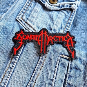Può includere: Una toppa ricamata nera e rossa con il testo "SONATA ARCTICA" in un font stilizzato.
