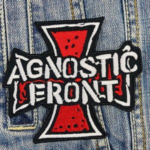 Puede incluir: Parche bordado en blanco y negro con las palabras "Agnostic Front" en fuente blanca sobre fondo negro. El parche presenta una cruz roja con contorno negro.