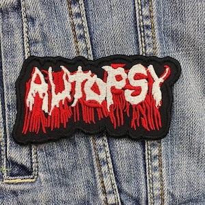 Könnte beinhalten: Schwarzer und roter gestickter Aufnäher mit dem Wort "AUTOPSY" in weißen Buchstaben.