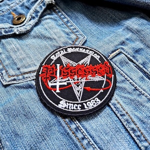 Puede incluir: Un parche redondo bordado en negro con texto e imágenes en rojo y blanco. El parche presenta las palabras "Total Possession" y "Since 1983". El parche está cosido a una chaqueta vaquera azul claro.