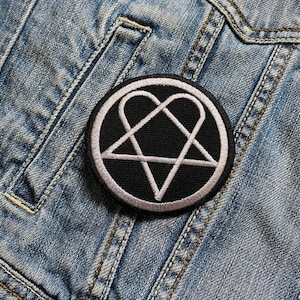 Könnte beinhalten: Ein gestickter Patch in Schwarz und Weiß mit einer Herzform in einem Pentagramm. Der Patch ist auf eine blaue Jeansjacke genäht.