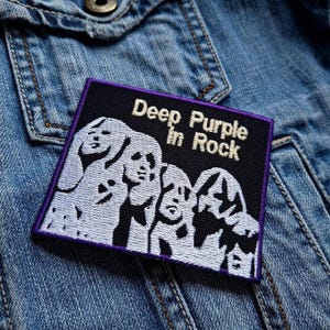 Op de afbeelding: Een geborduurde zwarte en witte patch met een paarse rand. De patch toont een silhouet van vier personen en de tekst "Deep Purple In Rock".