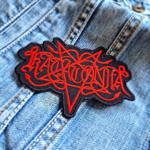 May include: A black and red embroidered patch with the word "LACONIA" in a stylized font.