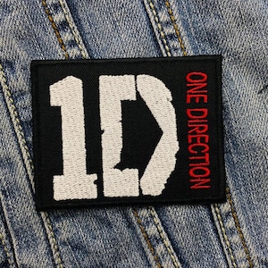 May include: Black and white embroidered patch with the text "1D" in white and "ONE DIRECTION" in red.