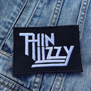 May include: Black and white embroidered patch with the text "Thin Lizzy" in white lettering on a black background.
