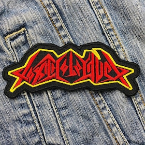 Peut inclure: Patch brodé noir, rouge et jaune avec le mot "SLAYER" dans une police stylisée.