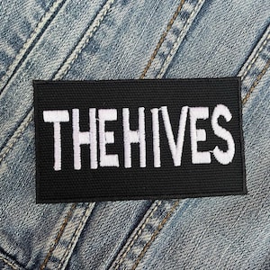 Könnte beinhalten: Schwarzer Stoff-Patch mit weiß gesticktem Text, der "THE HIVES" lautet.