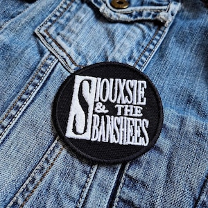 Op de afbeelding: Een geborduurde patch in zwart en wit met de tekst "Siouxsie & The Banshees" op een spijkerjack.