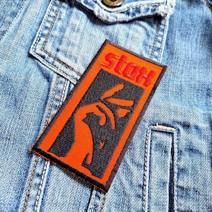 May include: Orange and black embroidered patch with the word "stay" in black lettering and a hand gesture.