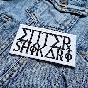 Puede incluir: Parche blanco bordado con letras negras que dice "ΣΠΙΤΣΣR SHΦΚΑΡΦ".