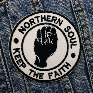 Może przedstawiać: Naszywka haftowana w kolorze białym i czarnym z uniesioną pięścią i tekstem "Northern Soul Keep The Faith".