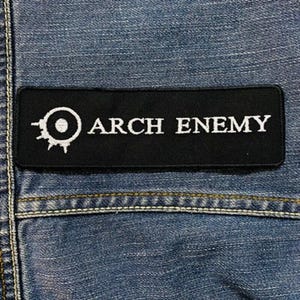 May include: Black and white embroidered patch with the band name "ARCH ENEMY" and a stylized circle with a dot in the center.