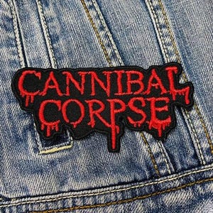 Puede incluir: Un parche bordado negro y rojo con las palabras "Cannibal Corpse" en una fuente de sangre que gotea.