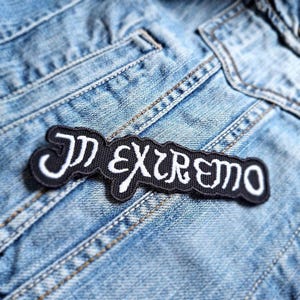 Könnte beinhalten: Ein schwarzer und weißer gestickter Aufnäher mit dem Text "In Extremo" auf einem blauen Jeansstoff.