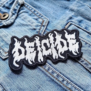May include: Black and white embroidered patch with the word "DECADE" in a stylized font. The patch is sewn onto a blue denim jacket.