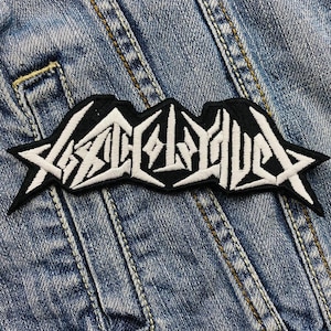May include: Black and white embroidered patch with the word "ARCH ENEMY" in a stylized font. The patch is sewn onto a blue denim jacket.
