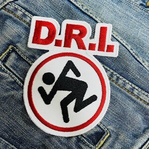Op de afbeelding: Een geborduurde patch in rood, wit en zwart met de tekst "D.R.I." en een gestileerd stickfiguur in een rode cirkel.