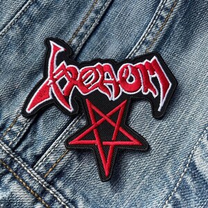 May include: Red and white embroidered patch with the word "Venom" in a stylized font, with a black pentagram underneath.