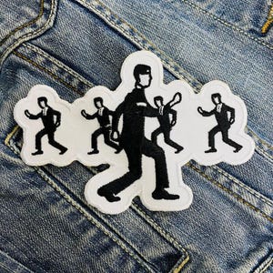 May include: White embroidered patch with five black figures in a line, all wearing suits and walking in the same direction. The figures are stylized and simple, with no facial features.