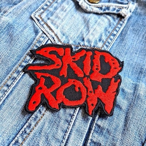 Puede incluir: Parche bordado rojo y negro con el nombre de la banda "SKID ROW" en una fuente estilizada.