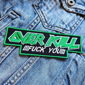 Può includere: Una toppa ricamata nera e verde con il testo "OVERKILL" in verde e "FUCK YOU" in bianco.