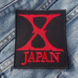 Op de afbeelding: Zwarte en rode geborduurde patch met de letter X en het woord "JAPAN" eronder.