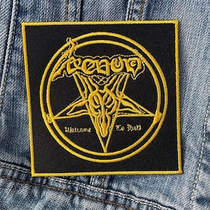 May include: Black and yellow embroidered patch with a pentagram and the word "VENOM" in a stylized font. The text "Welcome To Hell" is written below the pentagram.