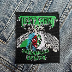 May include: Black and green embroidered patch with the band name "TESTAMENT" in white lettering and the album title "GREENHOUSE EFFECT" in white lettering. The patch features a green and white skull with a blue and red face.