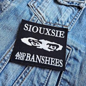 Könnte beinhalten: Schwarz-weiß gestickter Patch mit dem Text "Siouxsie and the Banshees" auf einer Jeansjacke.