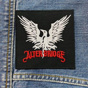Op de afbeelding: Zwarte en rode geborduurde patch met een wit vogelontwerp en de tekst "ALTER BRIDGE".