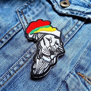 May include: A black and white embroidered patch of a lion's head wearing a red, green, and yellow hat. The patch is sewn onto a blue denim jacket.