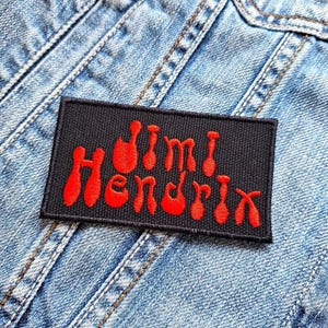 May include: A black fabric patch with the text "Jimi Hendrix" in red, styled to resemble guitar amplifiers.