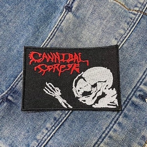 Può includere: Toppa ricamata in bianco e nero con il testo "Cannibal Corpse" in lettere rosse. La toppa presenta uno scheletro bianco con un teschio.