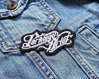 May include: A black and white embroidered patch with the text "Paralytic Riot" on a blue denim jacket.