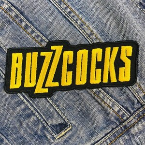 May include: A black and yellow embroidered patch with the word "BUZZCOCKS" in yellow lettering.