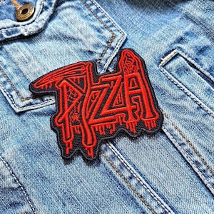 Puede incluir: Un parche bordado en rojo y negro con la palabra "RZA" en una fuente estilizada. El parche es rectangular con un borde negro y está colocado sobre una chaqueta vaquera.