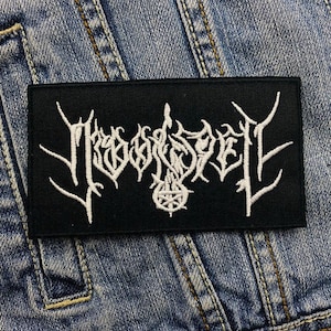 Può includere: Toppa ricamata nera con il testo bianco "MAYHEM" in un font stilizzato. La toppa è cucita su una giacca di jeans blu.