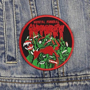 May include: A round patch with the words "MENTAL FUNERAL" in red above a green and red monster graphic. The patch is on a denim jacket.