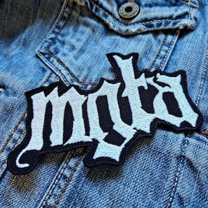 Pode incluir: Patch branco bordado "MYDA" em uma jaqueta jeans azul.