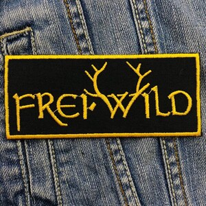 Könnte beinhalten: Schwarzer gestickter Patch mit gelber Naht. Der Patch zeigt den Text "FREI WILD" mit stilisierten Geweih.