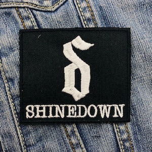 Könnte beinhalten: Schwarz-weiß gestickter Patch mit einem stilisierten "S" und dem Text "SHINEDOWN".