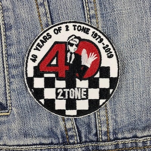 May include: A black and white checkered circle patch with a red number 40 and the text "40 Years of 2 Tone 1979-2019" and "2 Tone". A silhouette of a person in a suit is in the center of the patch.
