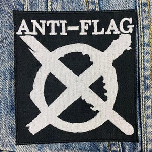 May include: Black and white embroidered patch with the text "ANTI-FLAG" and a white circle with a white X across it.