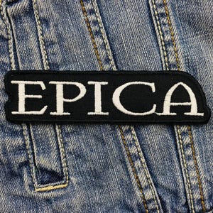 Puede incluir: Parche bordado en blanco y negro con la palabra "EPICA" en letras blancas sobre fondo negro.