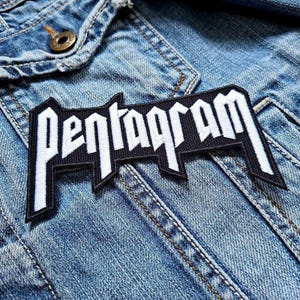 May include: A black and white embroidered patch with the word "Pentagram" in a bold, stylized font. The patch is sewn onto a blue denim jacket.